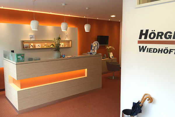 Moderner Empfangsbereich eines Hörakustikers mit beleuchtetem Tresen und Firmenlogo.
